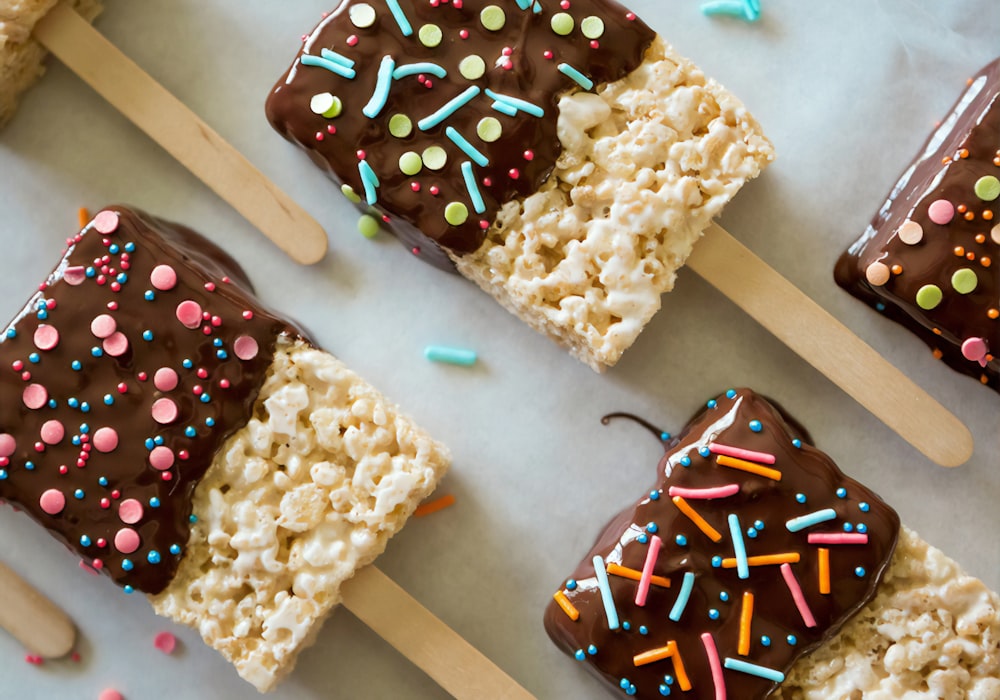 Chocolate covered treats topped with sprinkles, laid out on baking paper